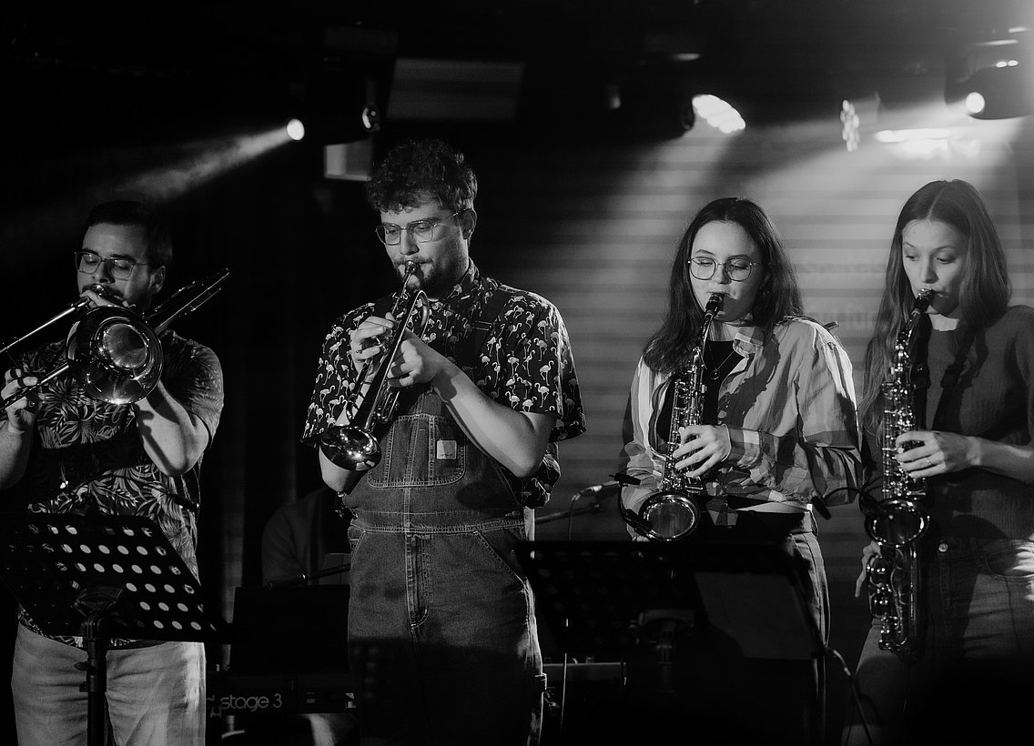 Vier Personen die auf der Bühne Blasinstrumente spielen in einer Reihe 